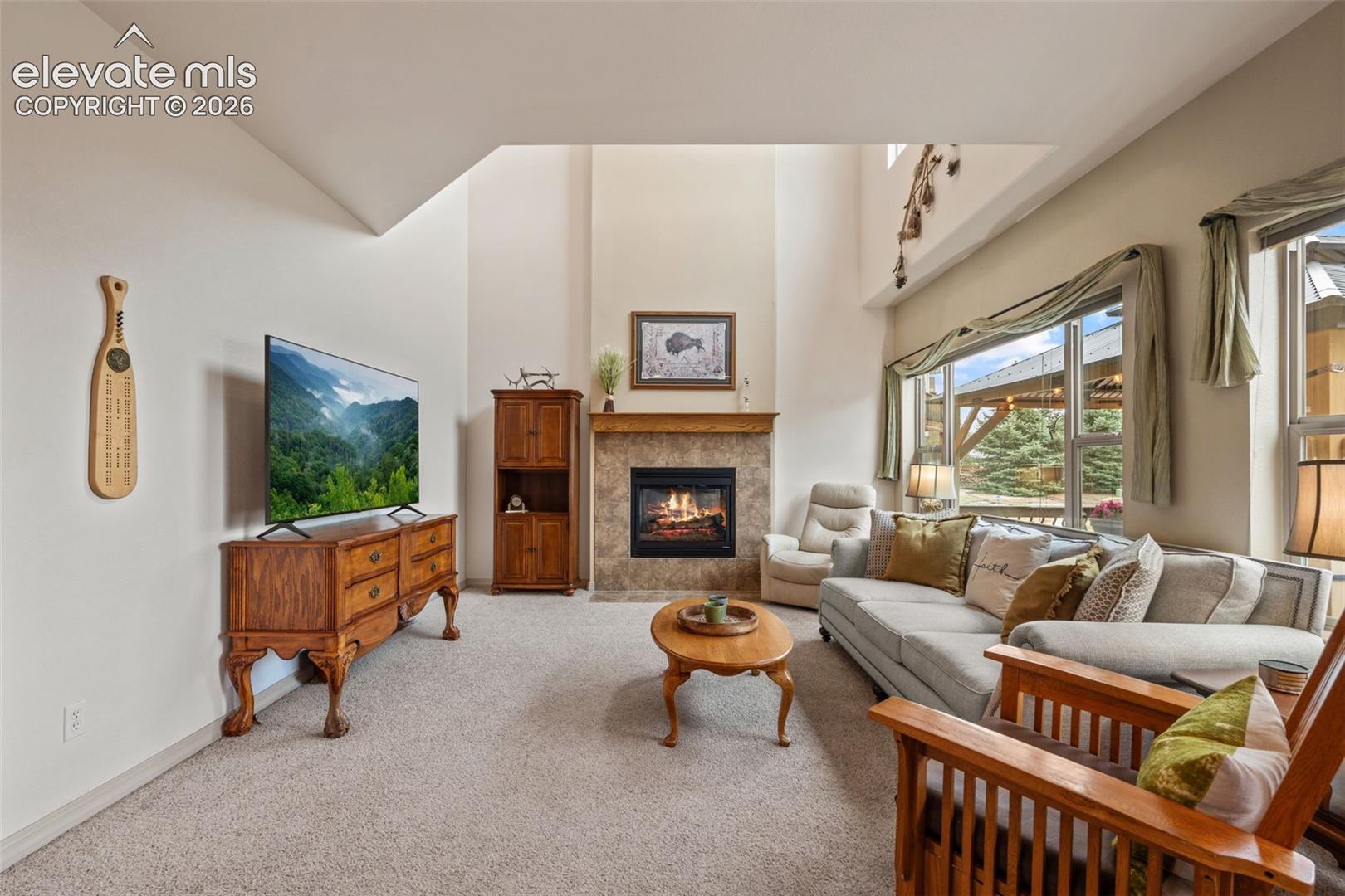 Living area featuring a stone-surround fireplace with wood mantel, large windows, and vaulted ceilings