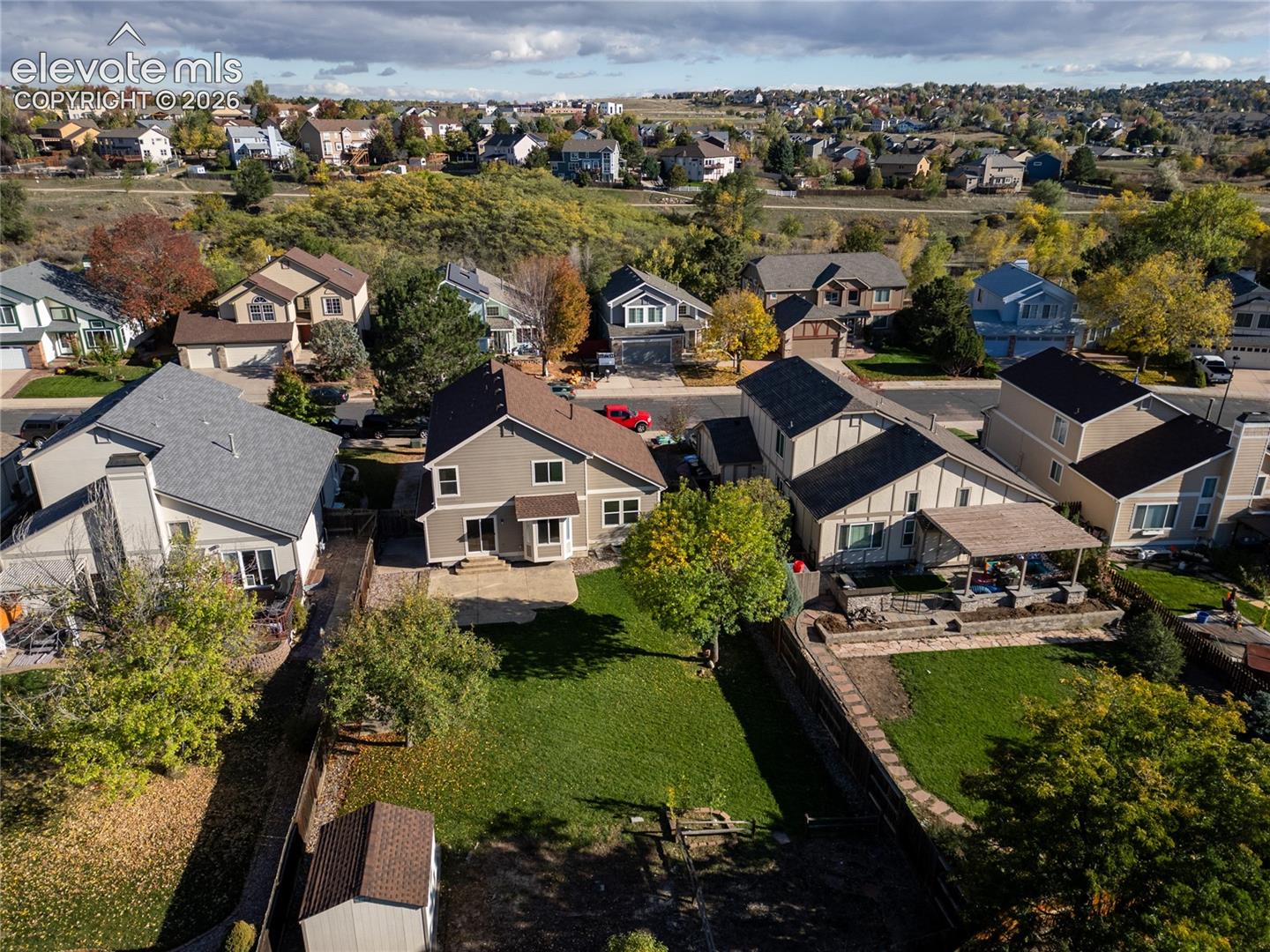 Aerial view of a residential property featuring an expansive lawn, rear patio, detached storage shed, and perimeter fencing