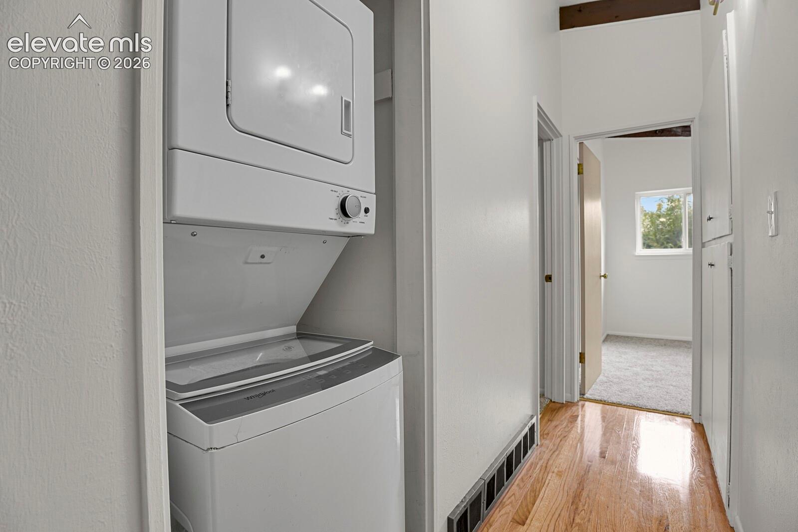 Laundry area featuring a stacked washer and dryer unit, wood-finish flooring, and built-in hallway cabinetry