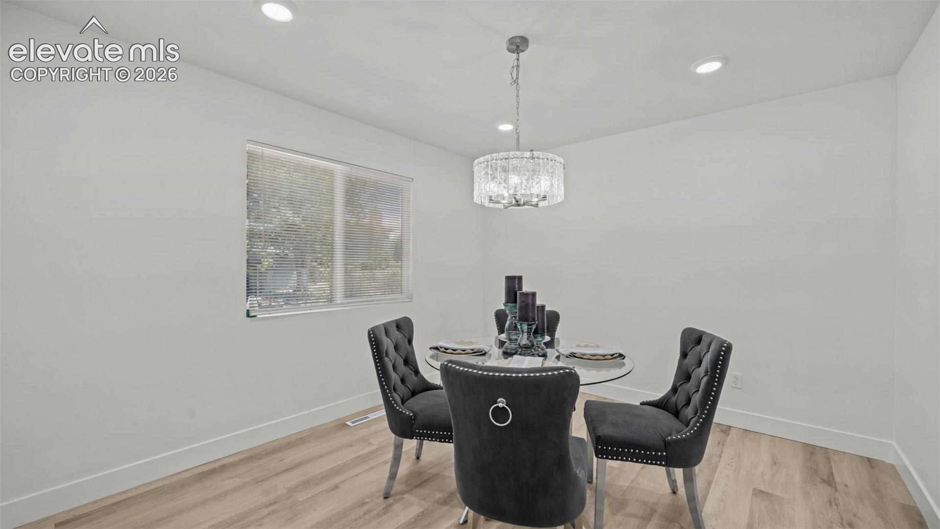 Recessed ceiling lighting, a contemporary chandelier, a window with horizontal blinds, and wood-finish flooring