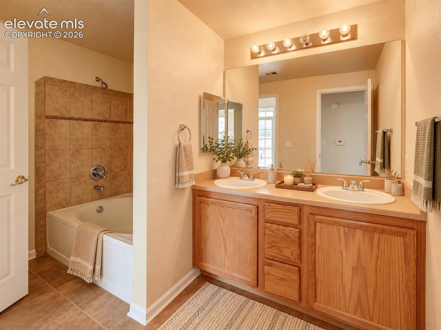 Double vanity with integrated sinks, wood cabinetry, large vanity mirror, and combined soaking tub and shower with tile surround