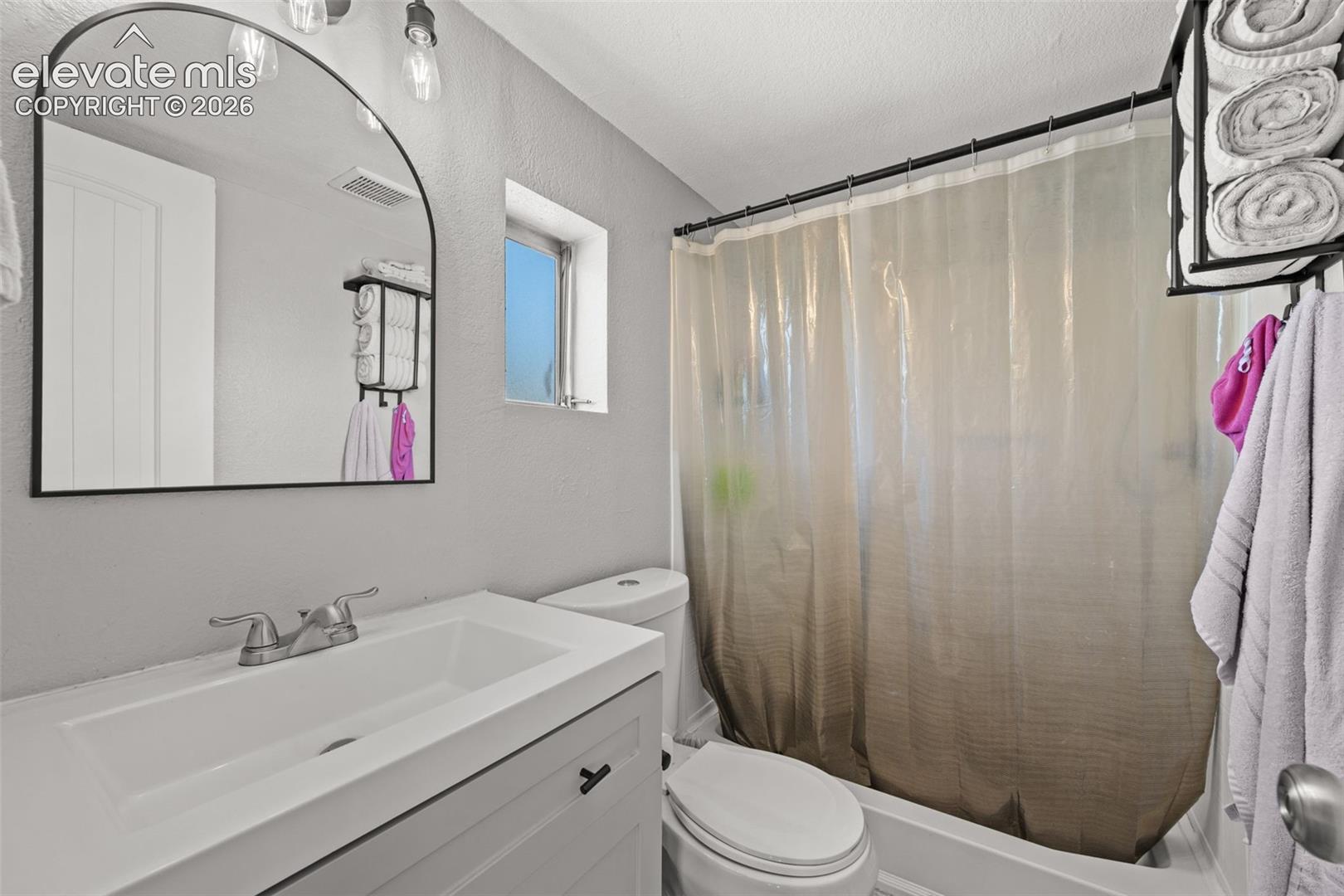 Bathroom featuring a white vanity with an integrated sink, arched mirror, dual-light vanity fixture, and a tub-shower combination with a black curtain rod