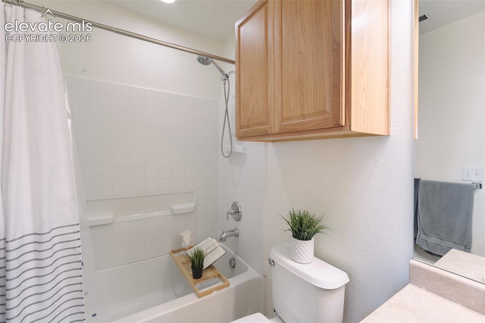 White subway tile shower surround with a built-in tub, recessed lighting, and a wood-finish overhead cabinet