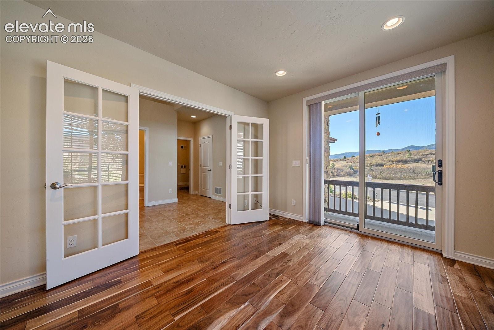 Interior space featuring wood-finish flooring, double glass-paneled French doors, recessed ceiling lighting, and sliding glass doors opening to an exterior balcony with a mountainous landscape