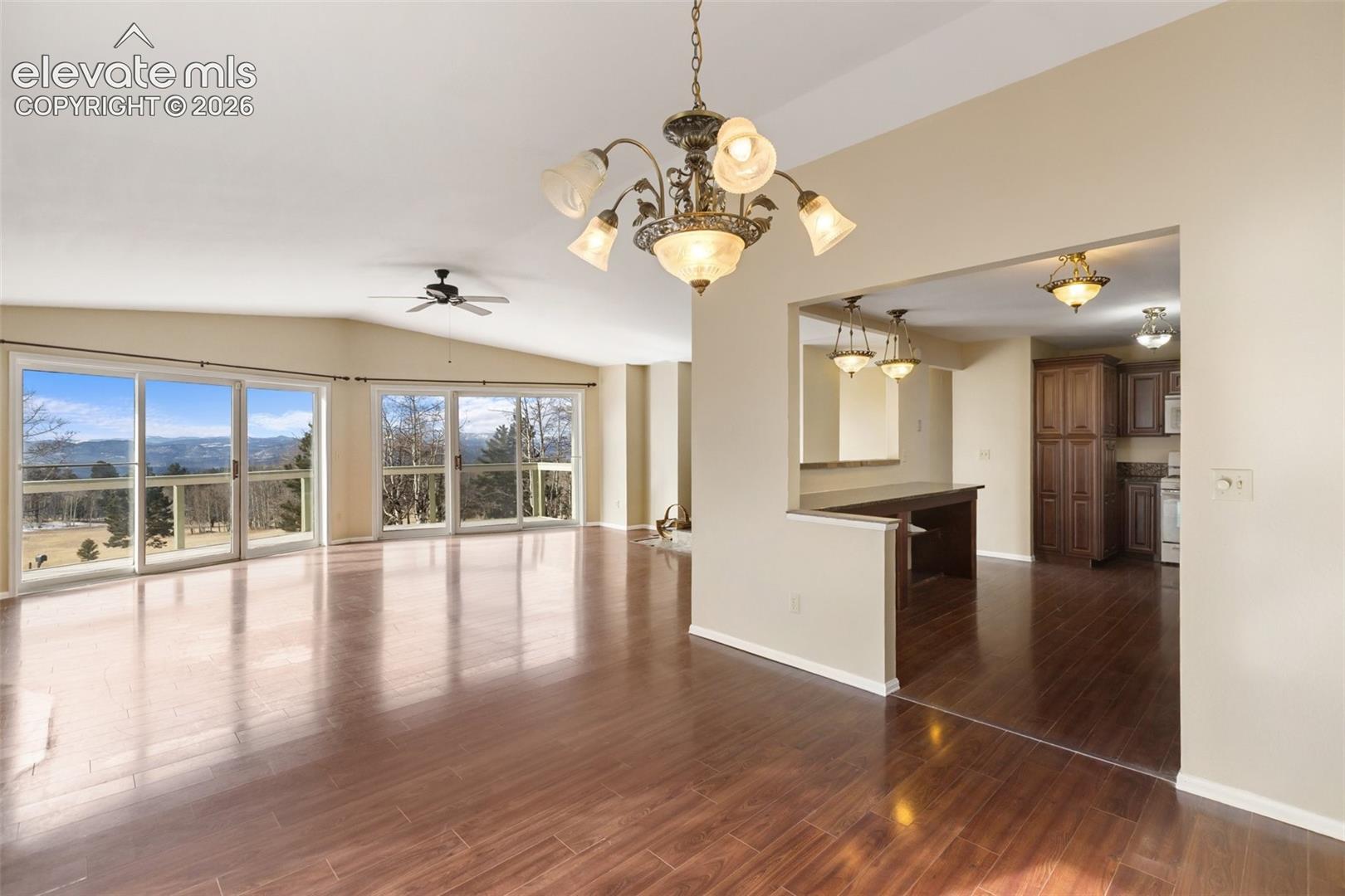 Open-concept living area featuring wood-finish flooring, vaulted ceiling, and multiple sliding glass doors