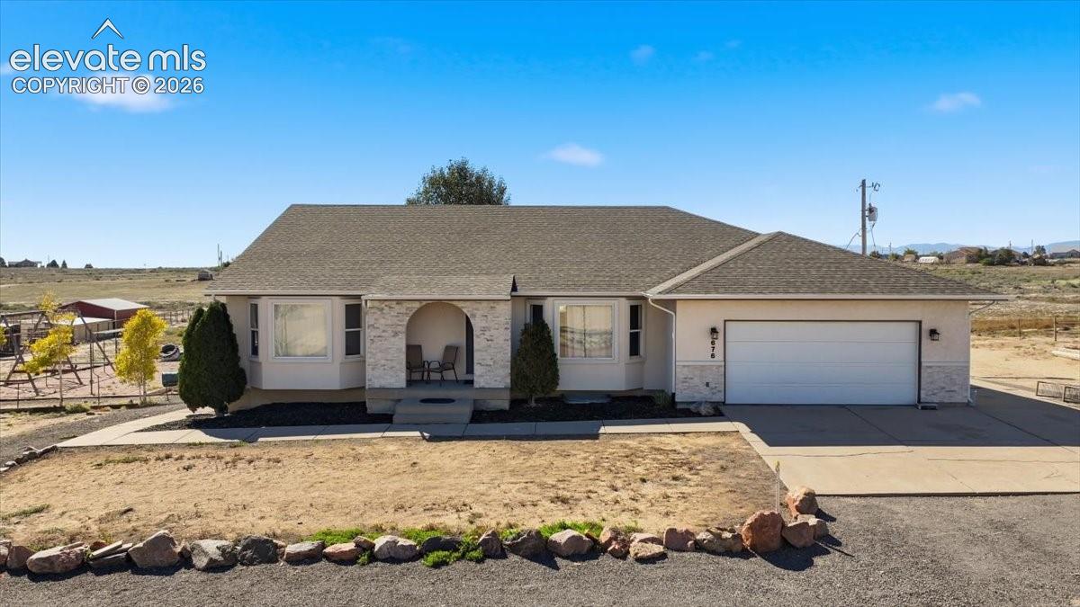 Single-story residence featuring a stucco exterior, arched covered entryway with stone masonry accents, shingle roof, and an attached two-car garage