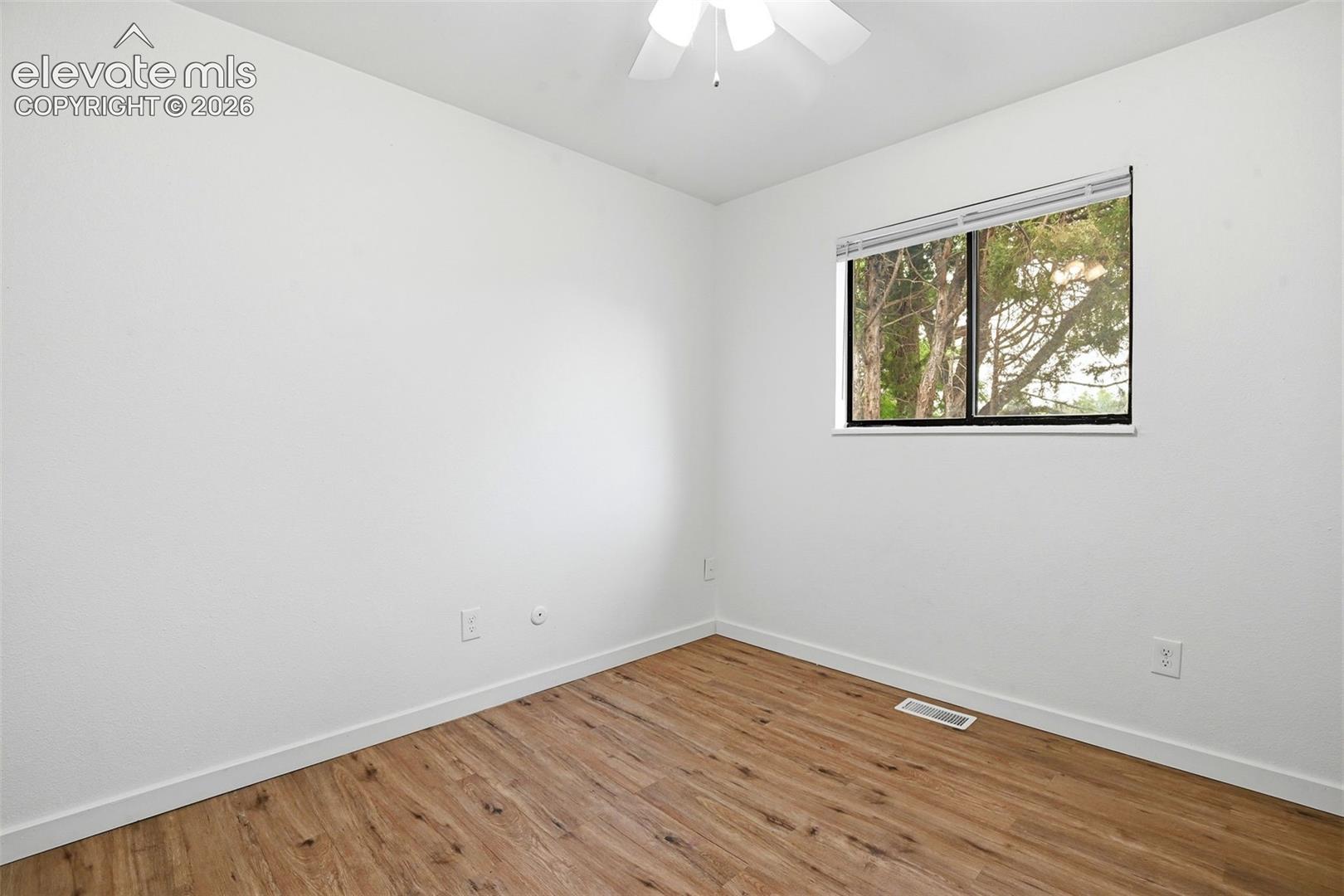 Wood-finish flooring, white walls, and a window with horizontal blinds