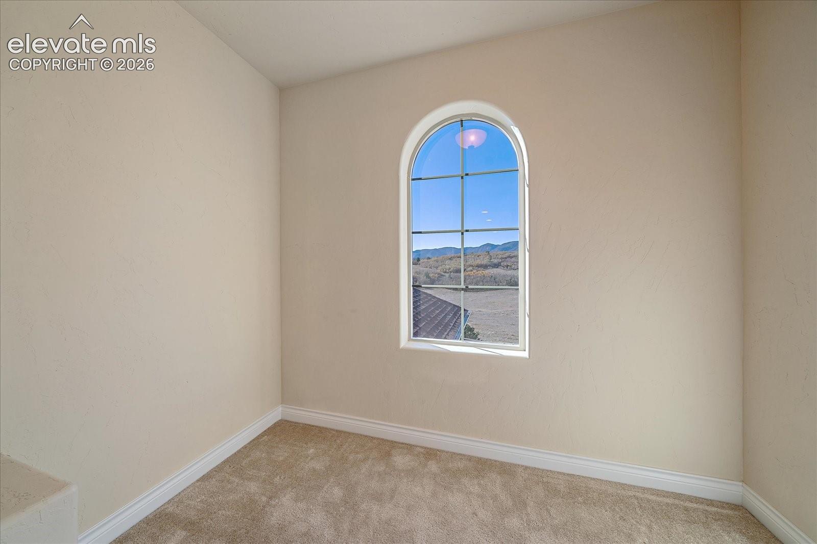 Interior space featuring neutral-toned walls, wall-to-wall carpeting, and an arched window with a grid pane design framing a mountain backdrop