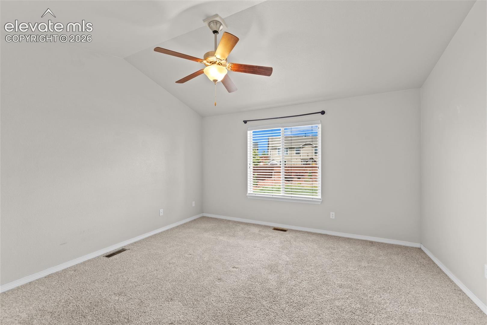 Bright bedroom featuring neutral carpeting, a ceiling fan with integrated lighting, and a large window with plantation shutters allowing natural light throughout the space