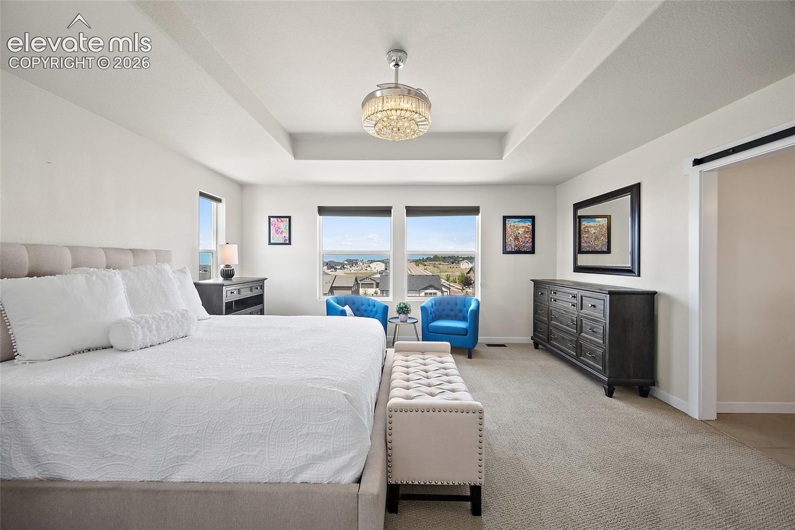 Tray ceiling with a decorative chandelier, dual windows, and carpeted flooring