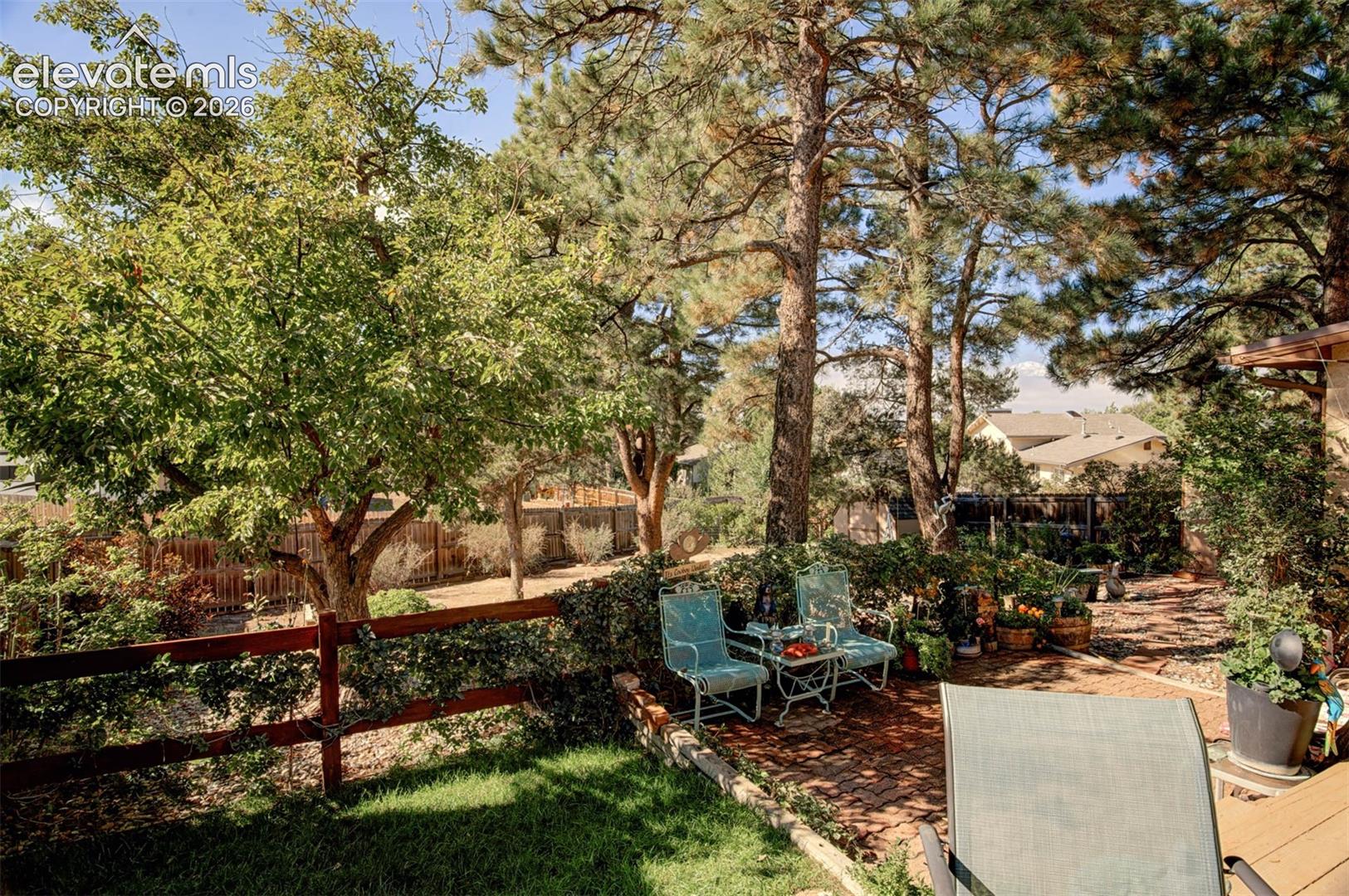 Terraced backyard with mature trees, a brick paver patio, wood fencing, and a grassy area