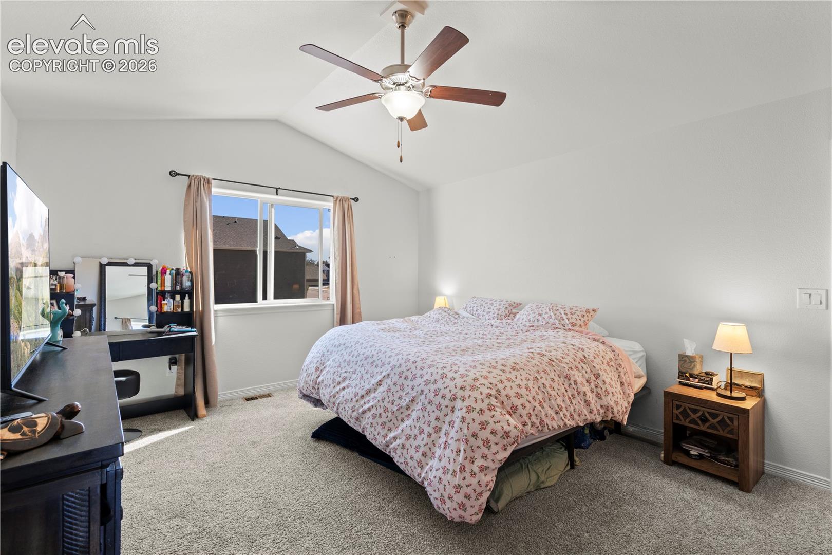 Vaulted ceiling featuring a central ceiling fan with integrated lighting and carpeted flooring