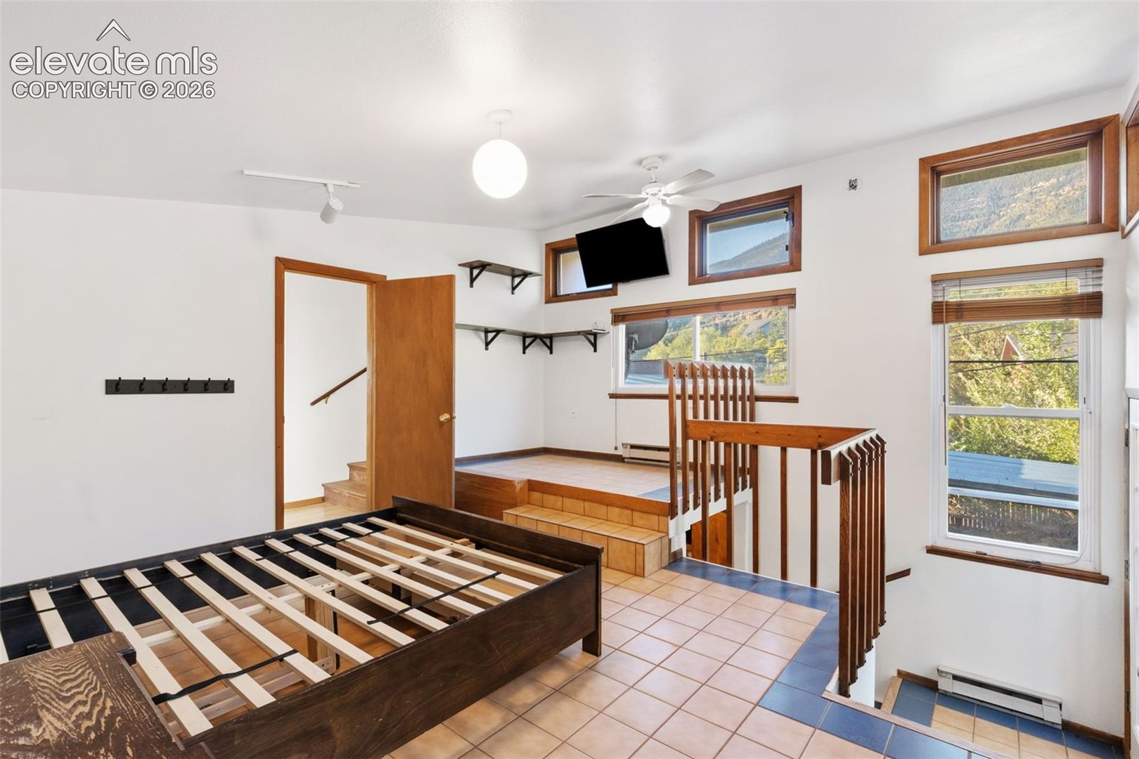 Multi-level interior featuring tile flooring, raised platform area, wood railing, and windows with wood trim