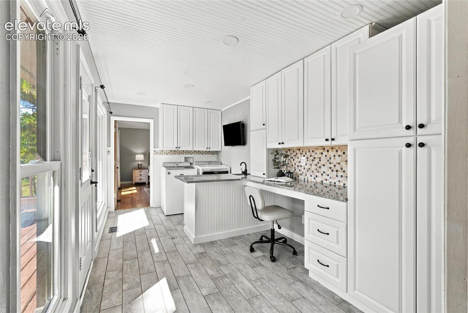 White shaker-style cabinetry with matte black hardware, mosaic tile backsplash, granite-finish countertops, wood-finish tile flooring, and beadboard ceiling
