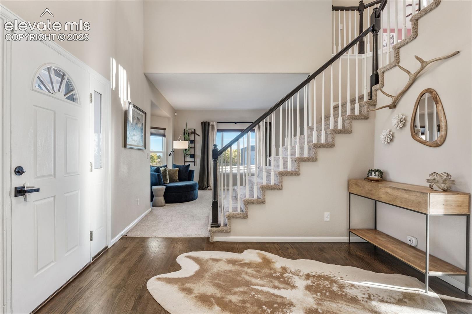 Foyer featuring vaulted ceilings, wood-finish flooring, and a staircase with white balusters and dark-stained handrails