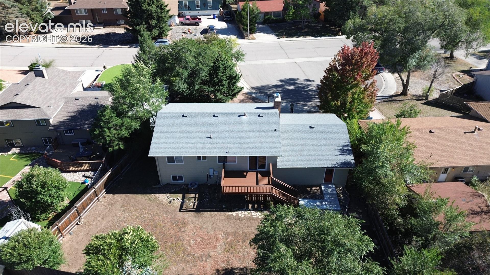 Aerial view featuring a multi-level home with a composition shingle roof, a raised wood-finish deck with integrated stairs, and a fenced backyard