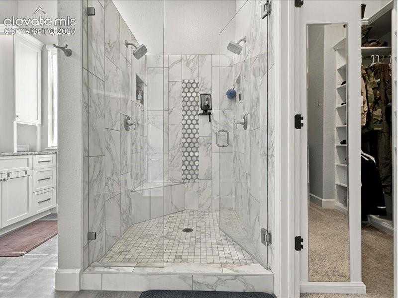 Spacious walk-in shower with glass enclosure, dual shower heads, integrated bench, and marble-finish tile
