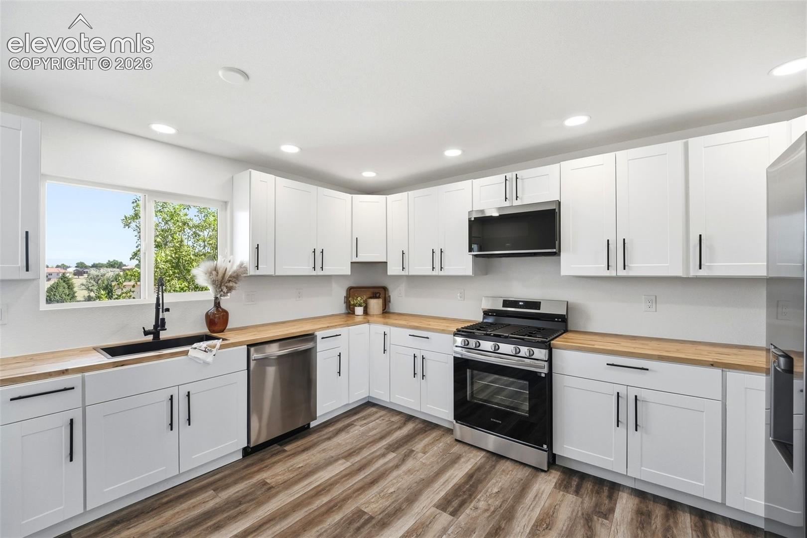 Kitchen featuring white shaker cabinetry with matte black hardware, wood-finish countertops, and stainless steel appliances