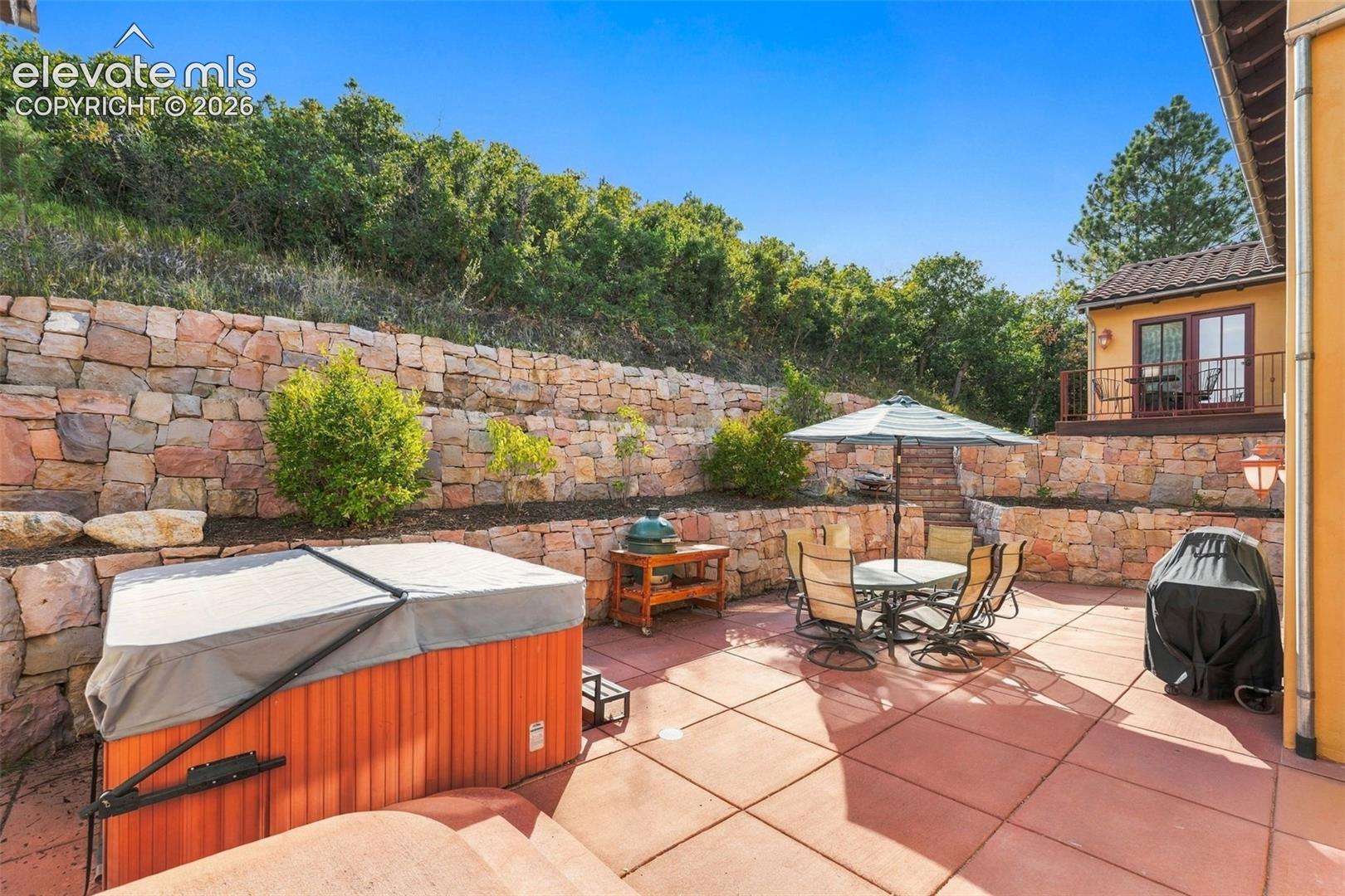 Private outdoor patio featuring a hot tub, stone retaining walls, and terraced landscaping