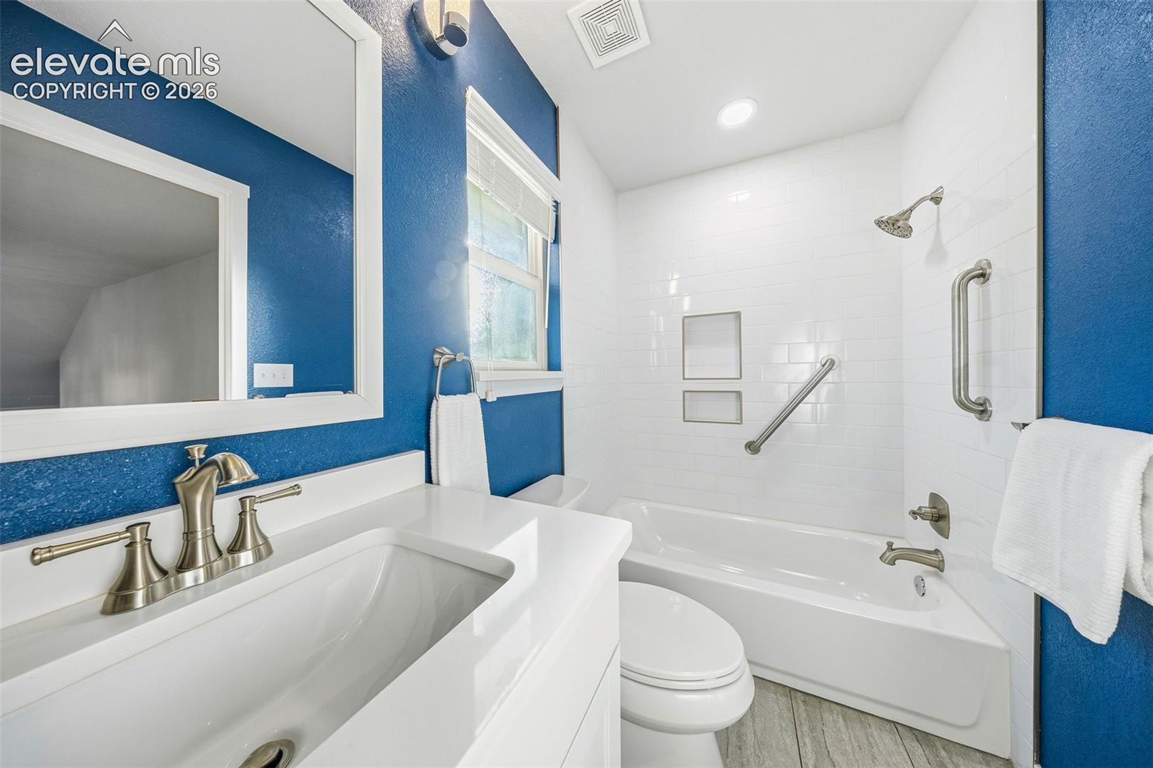 Bathroom featuring a white vanity with a rectangular sink, brushed nickel faucet, subway-tiled shower surround with dual recessed niches, and wood-finish flooring