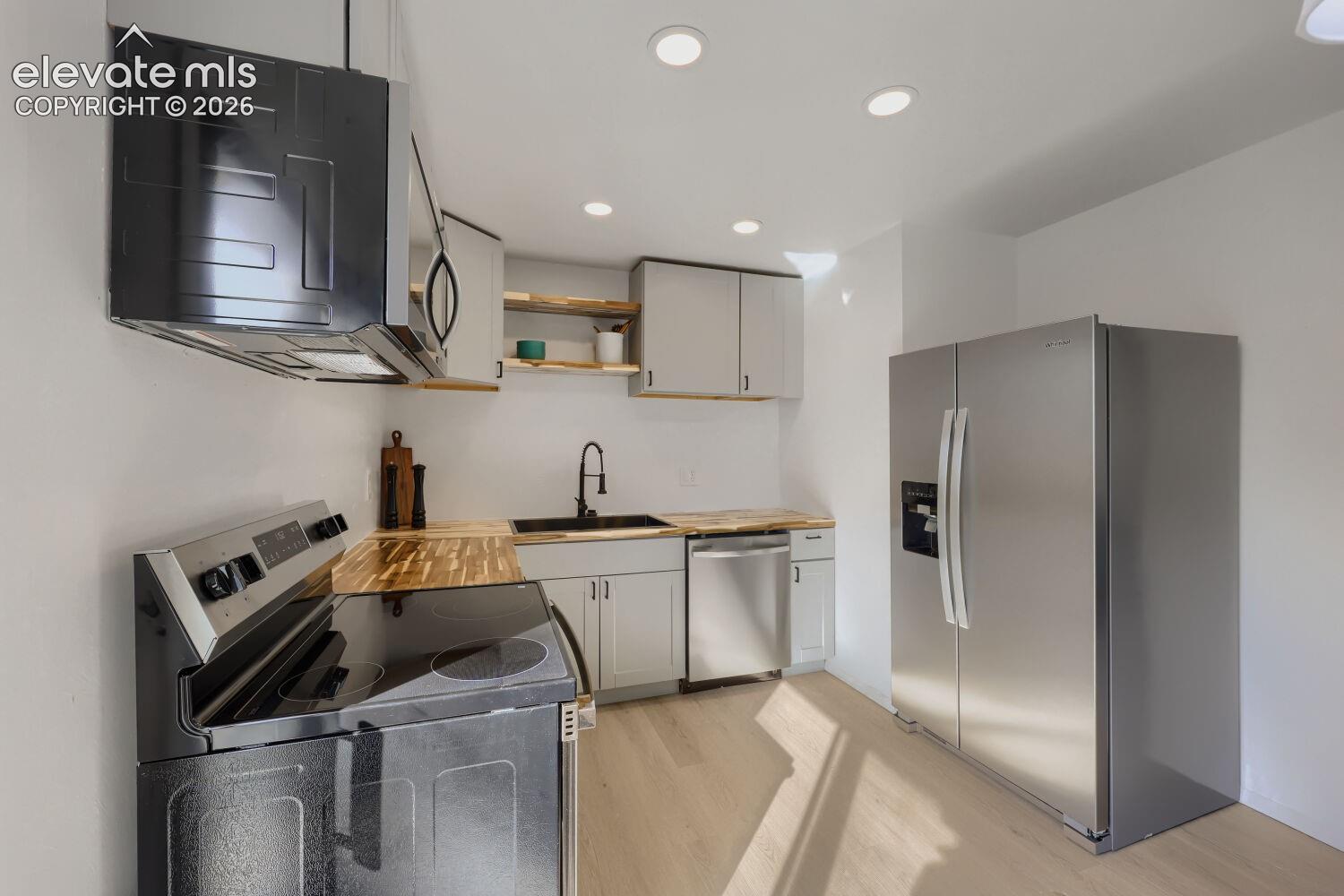 Kitchen featuring wood-finish countertops, stainless steel appliances, recessed lighting, shaker-style cabinetry, and wood-finish flooring