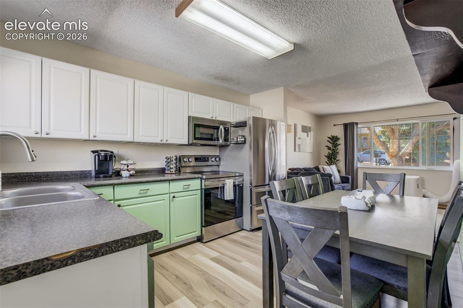 Kitchen featuring white upper cabinetry, green lower cabinetry, and stainless steel appliances