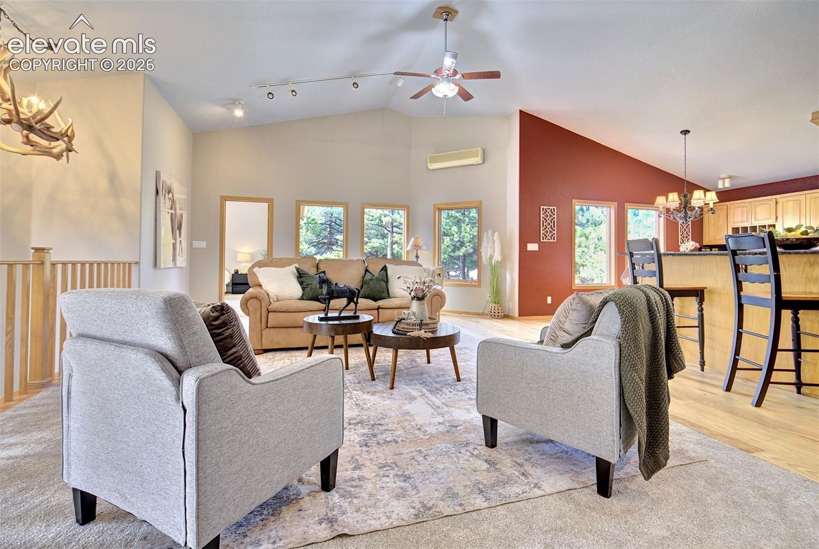 Vaulted ceilings, track lighting, ceiling fan, accent wall, and wood-finish flooring