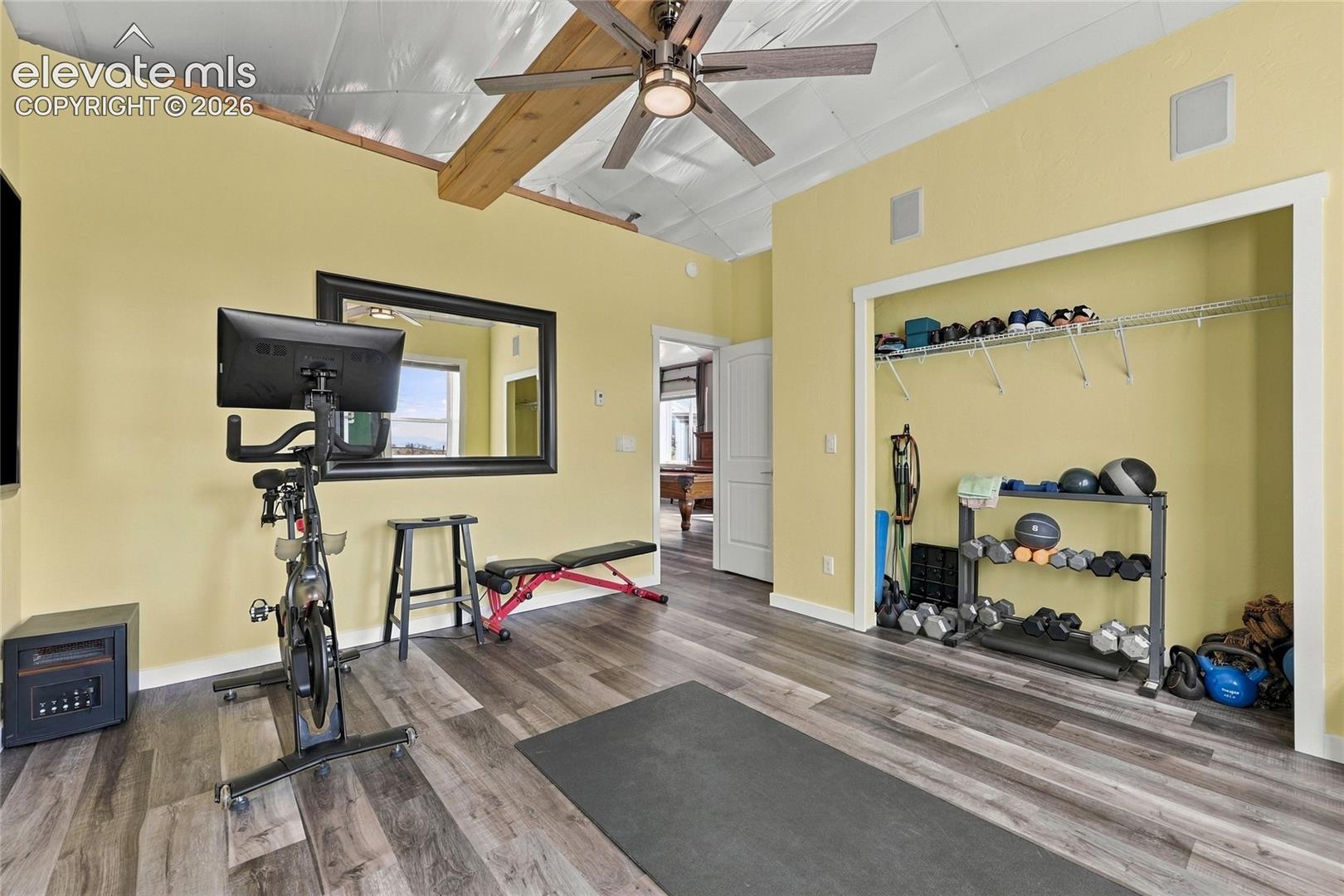Vaulted ceiling featuring an exposed wood beam, wood-finish flooring, ceiling fan with integrated lighting, and a walk-in closet with built-in wire shelving