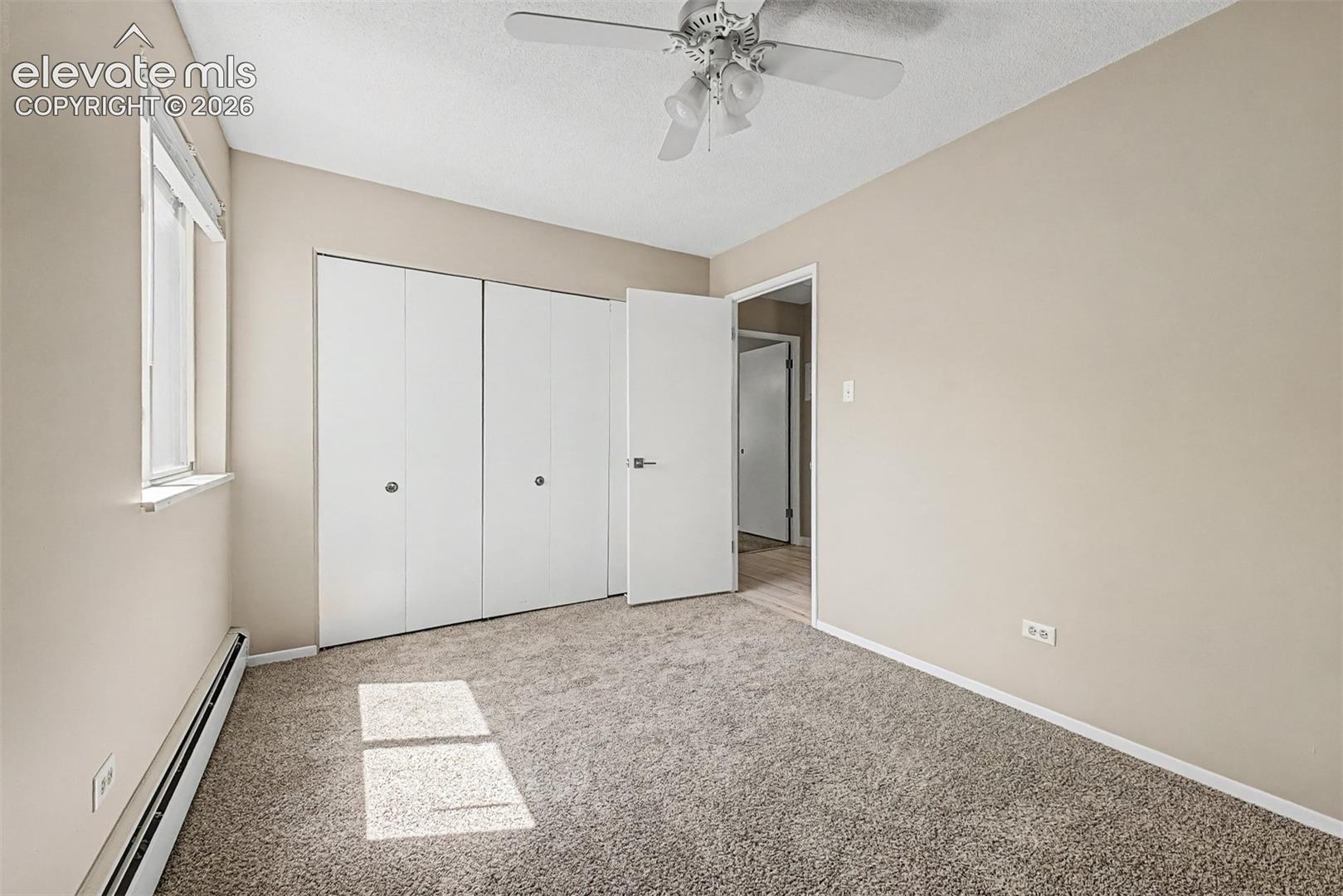 Neutral-toned room featuring a window with white trim, built-in bi-fold closet doors, and light-colored carpeting