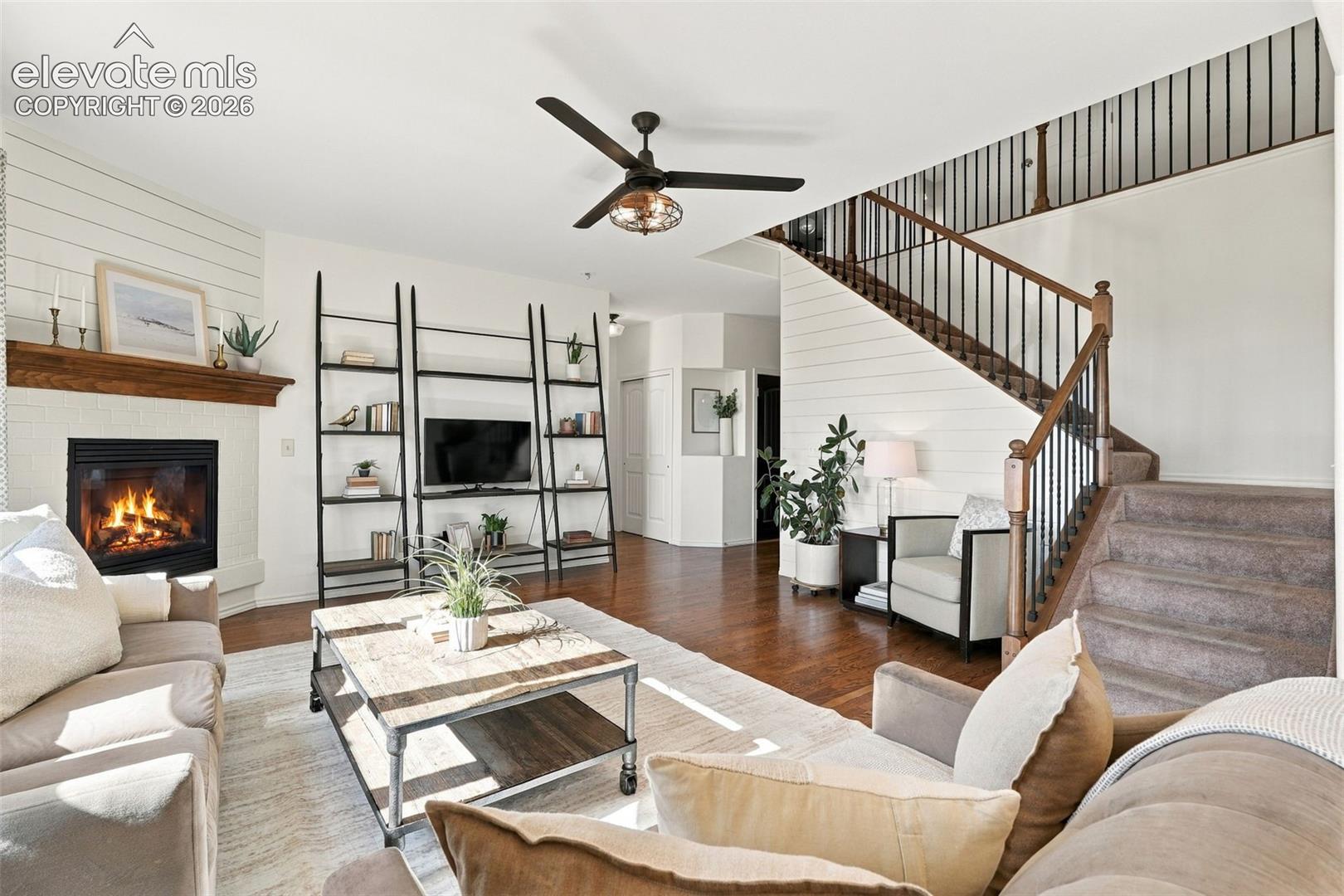 Living area featuring wood-finish flooring, a fireplace with a wood mantel, shiplap wall accents, and a staircase with metal balusters