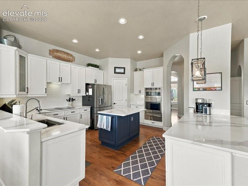 White shaker cabinetry, stainless steel appliances, wood-finish flooring, recessed lighting, and a kitchen island with a contrasting base