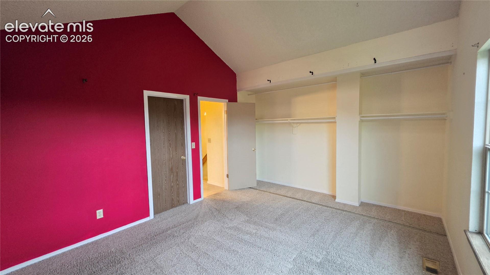 Vaulted ceiling, wall-to-wall carpeting, open shelving with hanging rods, and a window for natural light