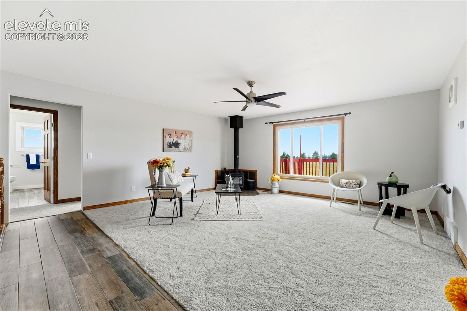 Spacious living area featuring light-colored carpeting, a wood-burning stove, and a ceiling fan