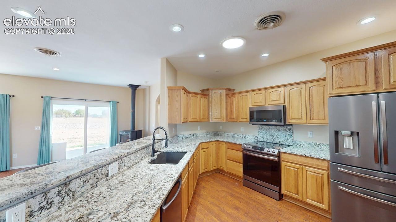 Kitchen featuring wood-finish flooring, light wood cabinetry, stainless steel appliances, and ample counter space with a breakfast bar