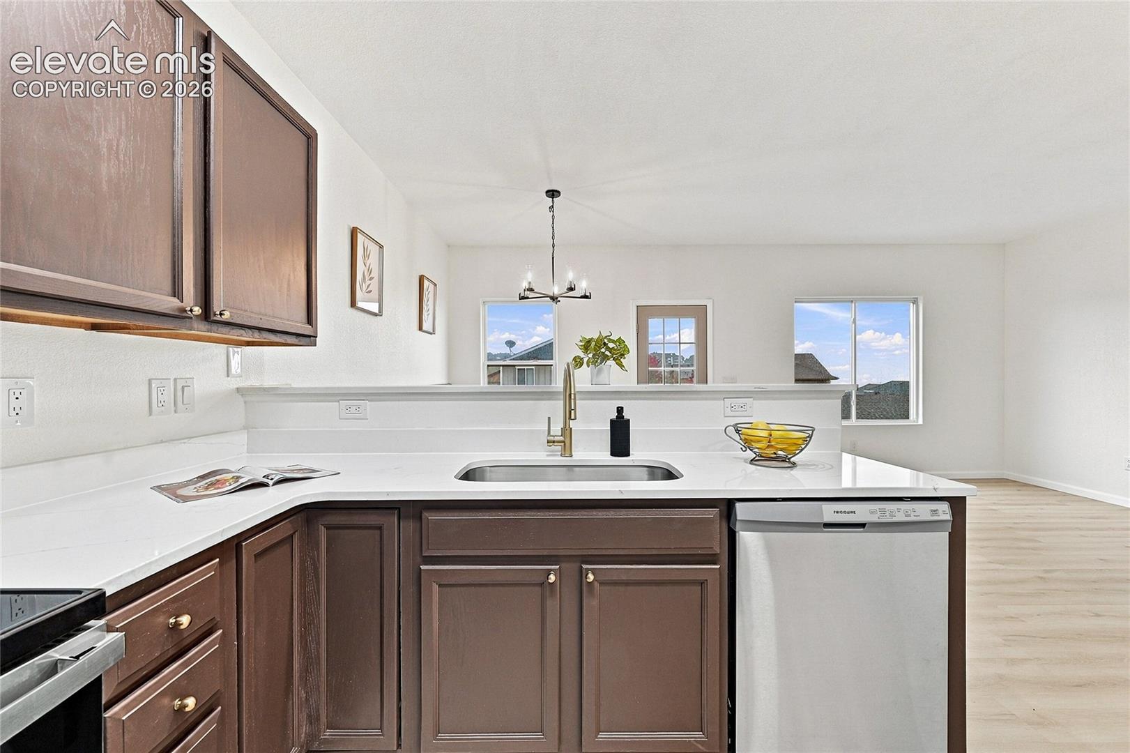 Kitchen featuring dark wood cabinetry, white countertops, stainless steel sink with gold-tone faucet, light-toned flooring, and a multi-light chandelier