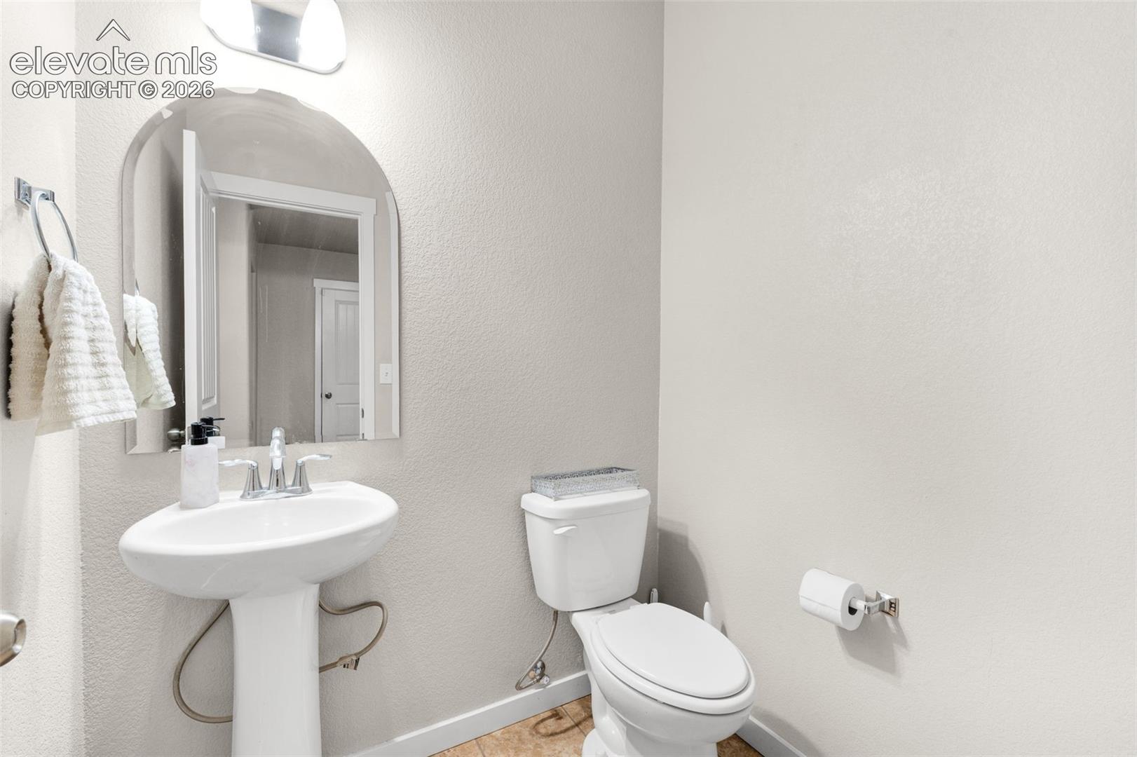 Pedestal sink featuring a chrome faucet, arched wall-mounted mirror, overhead light fixture, and standard-height toilet