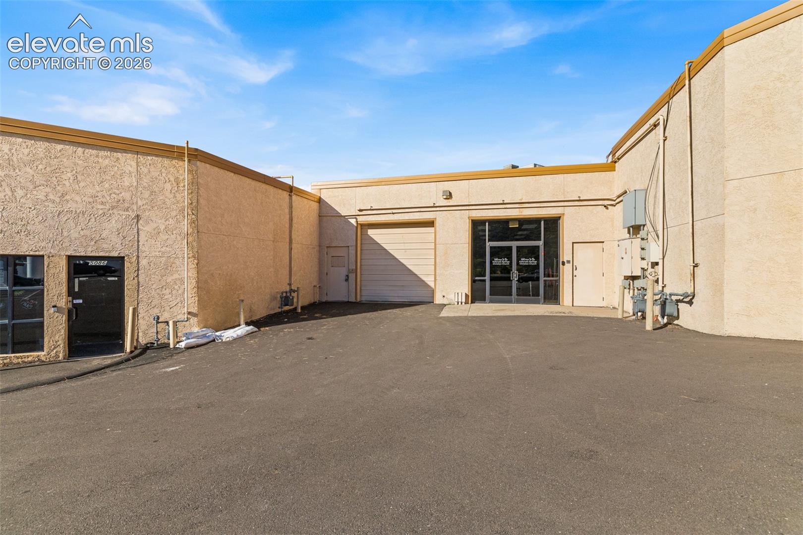Commercial exterior featuring stucco finish, roll-up bay door, double glass entry doors, and paved loading area
