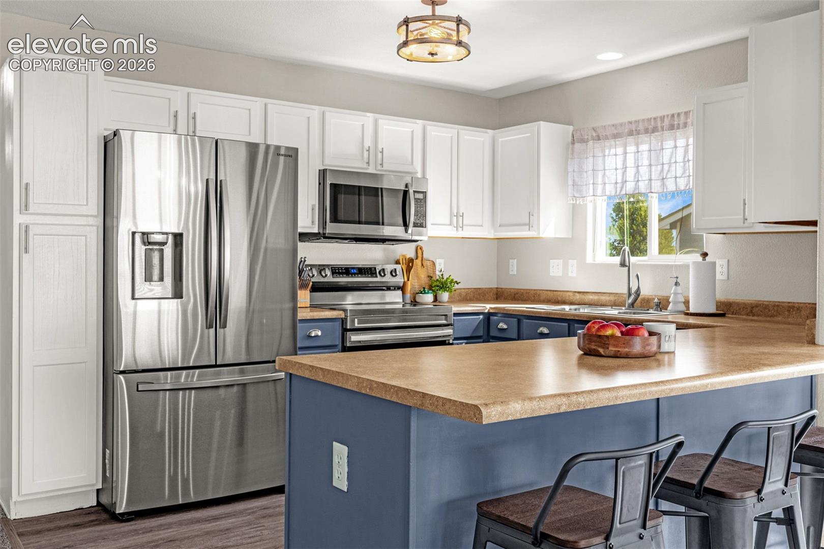 Kitchen featuring stainless steel appliances, white upper cabinetry, blue lower cabinetry, a kitchen island, and wood-finish flooring