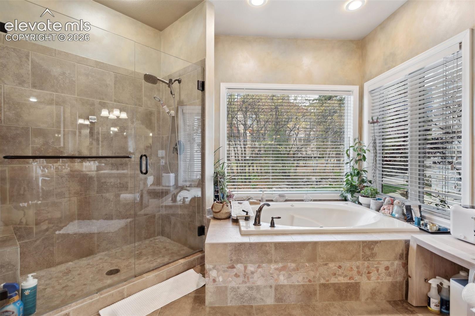 Spacious bathroom featuring an oversized soaking tub with surrounding windows and a separate glass-enclosed shower