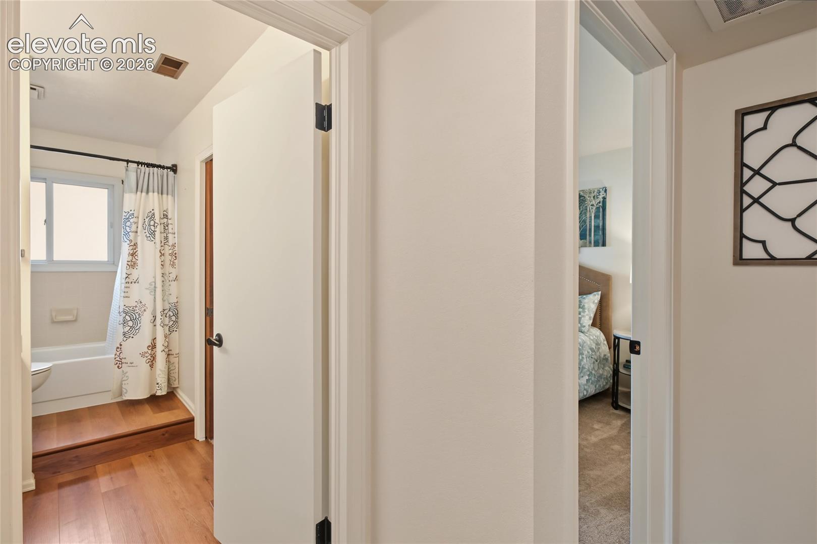 Wood-finish flooring leading to a full bathroom with a white tub and a window