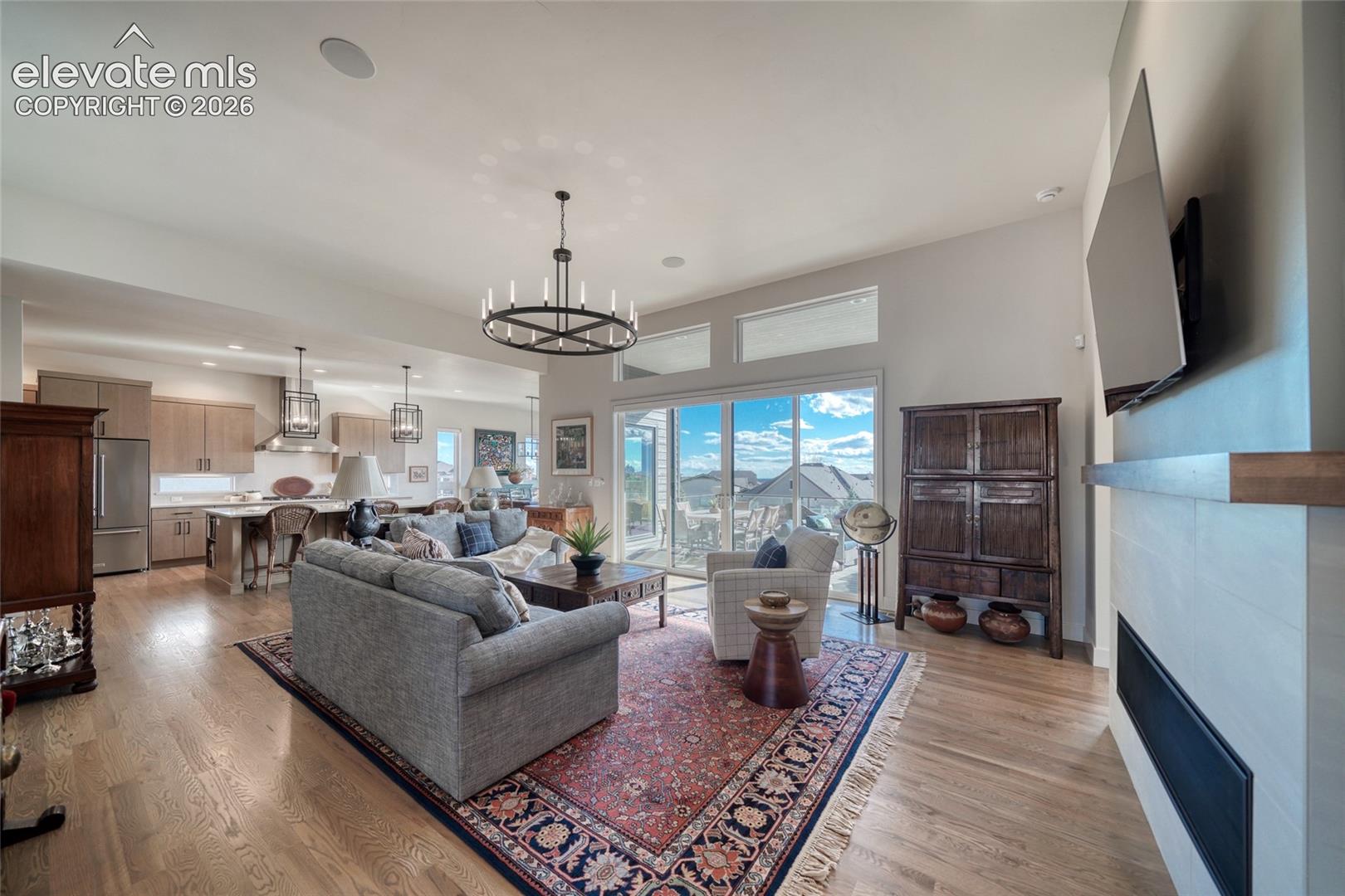 Open-concept interior featuring wood-finish flooring, a contemporary linear fireplace with a wood mantel, a large multi-light chandelier, and expansive sliding glass doors