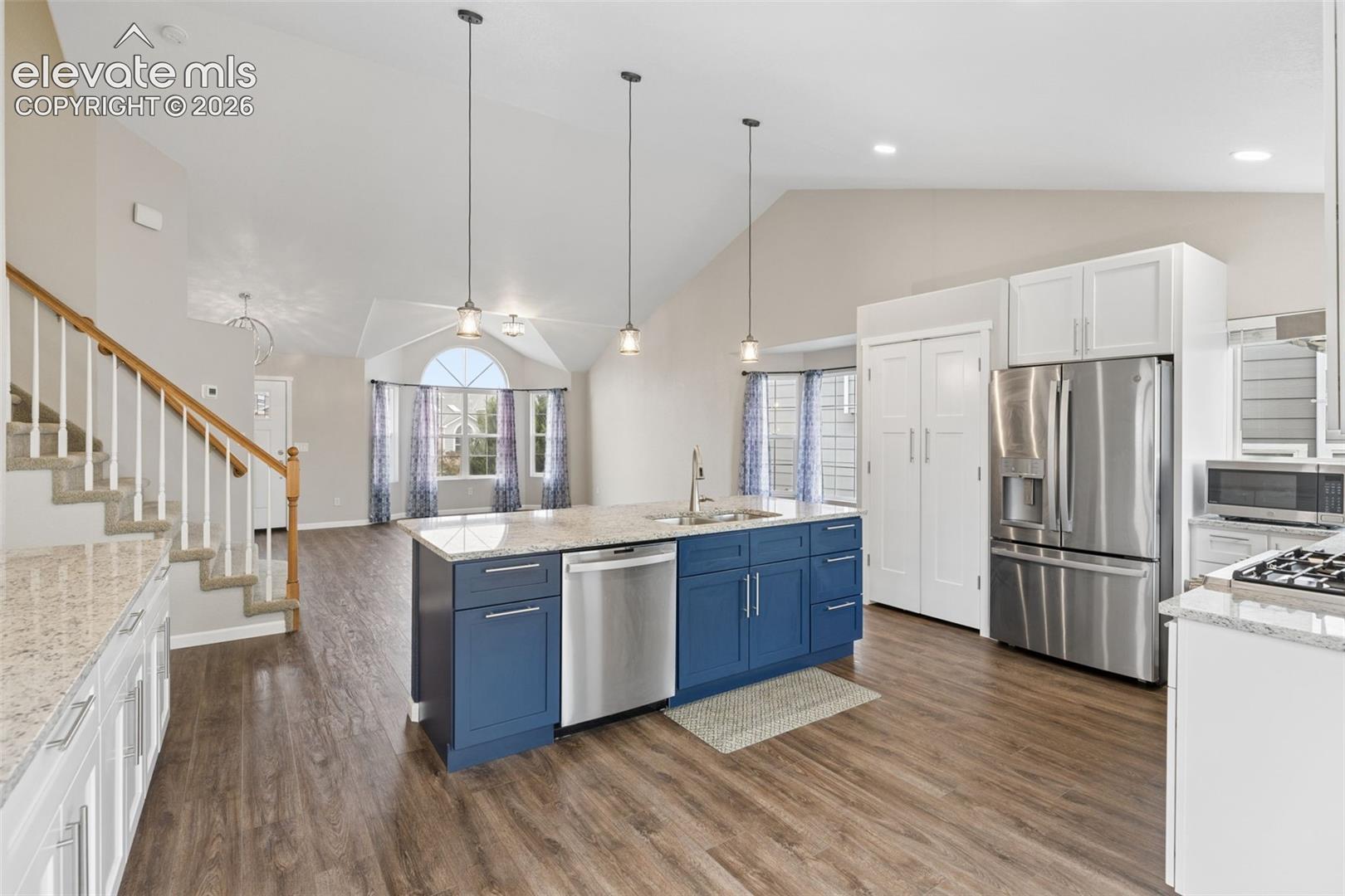 Kitchen featuring a large central island with blue cabinetry, stone-finish countertops, stainless steel appliances, wood-finish flooring, and vaulted ceilings
