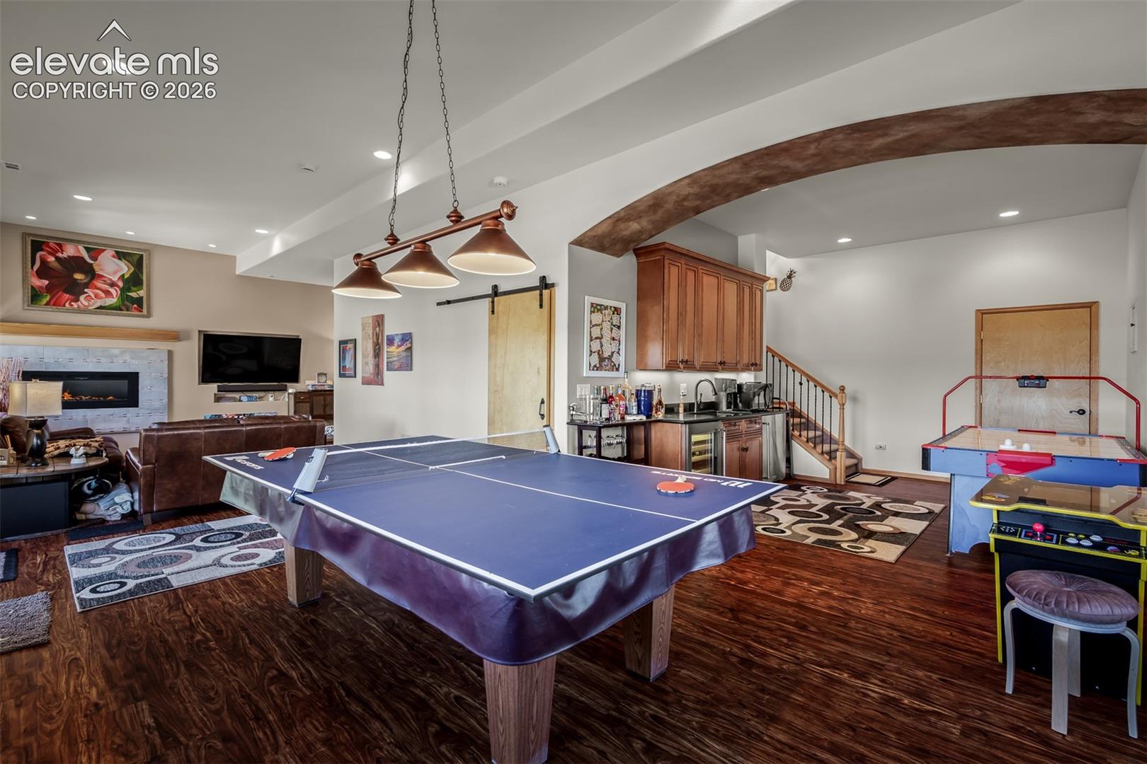 Spacious recreational area featuring wood-finish flooring, a built-in wet bar with wood cabinetry, and an arched ceiling detail.