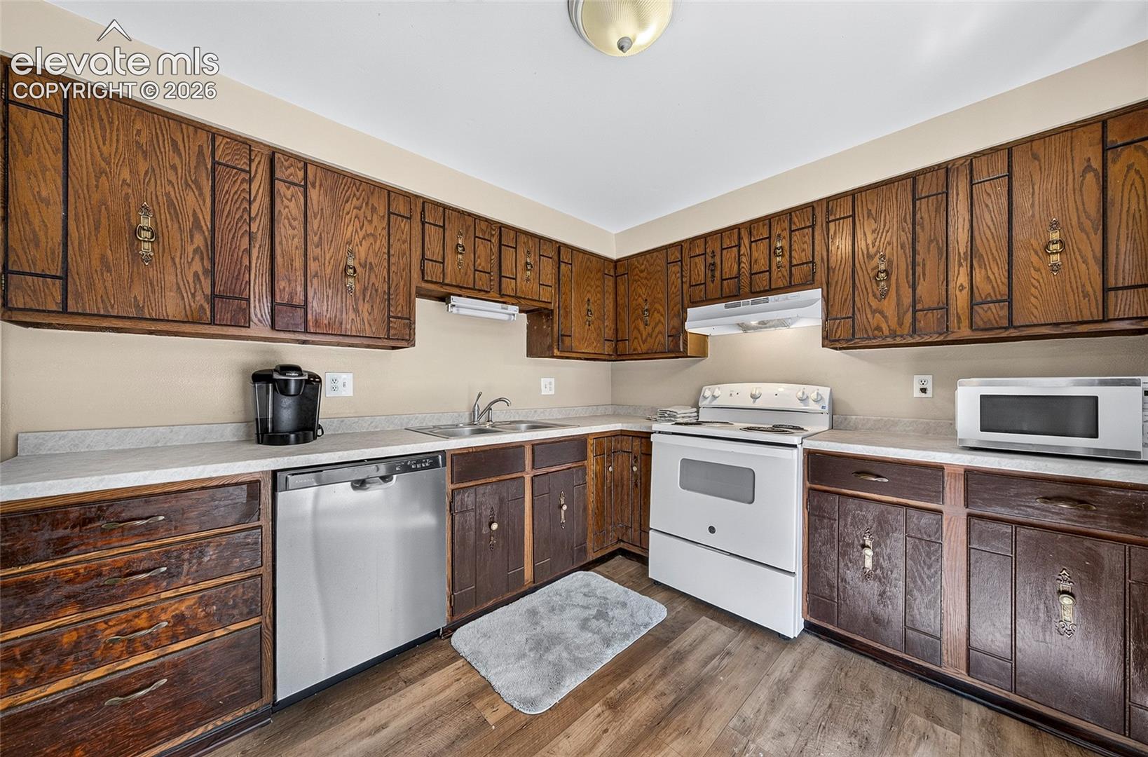 Kitchen featuring stained wood cabinetry, stainless steel dishwasher, white range with integrated hood, and wood-finish flooring