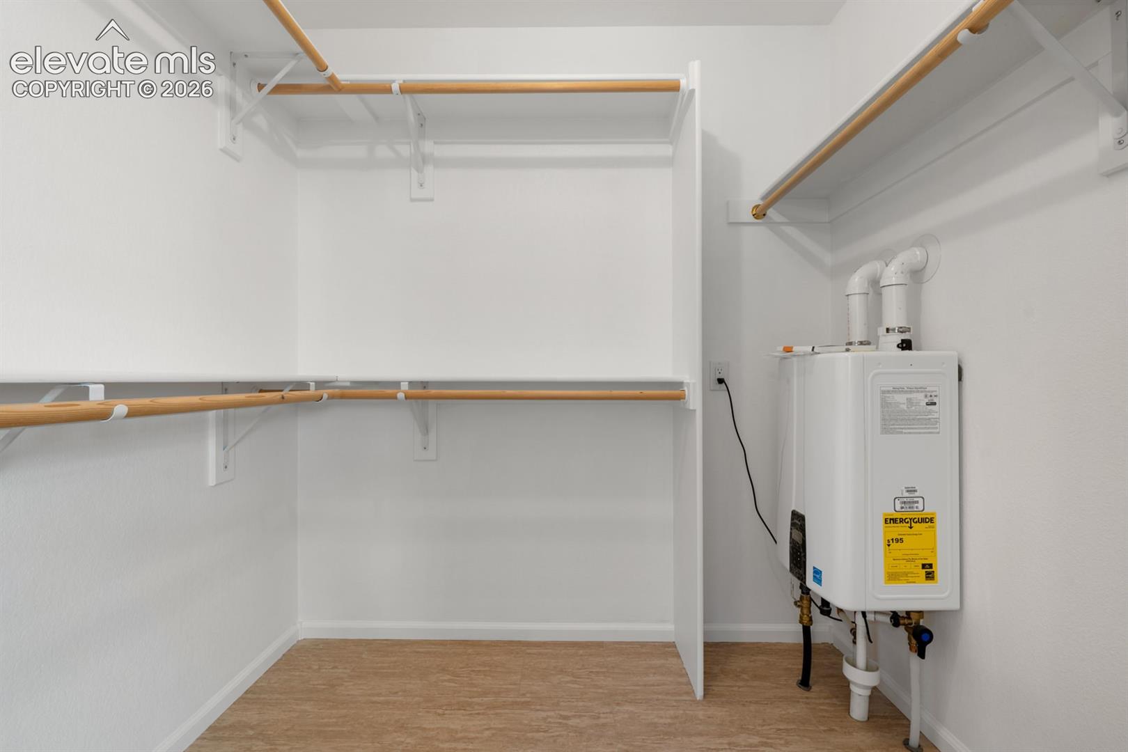 Storage area featuring white built-in shelving, wood-finish hanging rods, and a tankless water heater