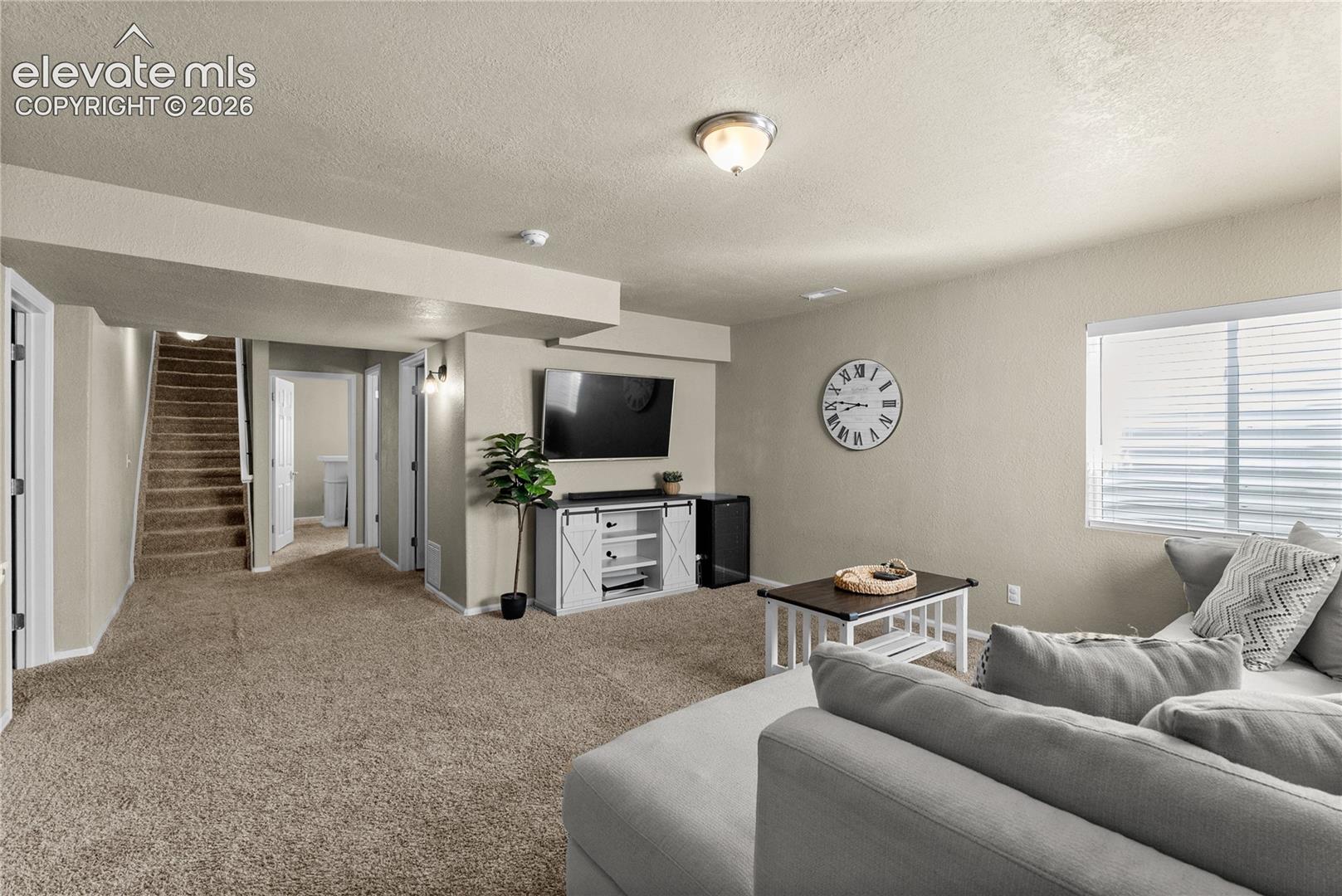 Carpeted living area featuring a window with blinds, recessed lighting, and wall-mounted light fixtures