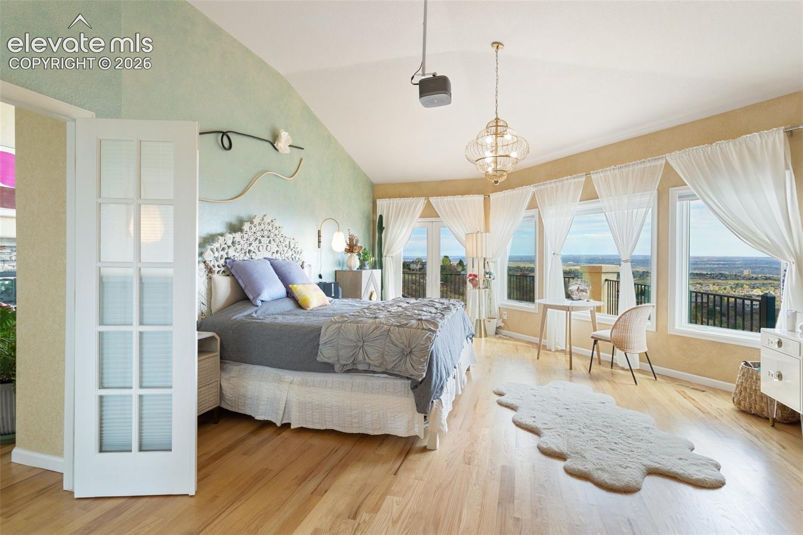 Spacious bedroom featuring light wood-finish flooring, a vaulted ceiling, and an ornate pendant light fixture