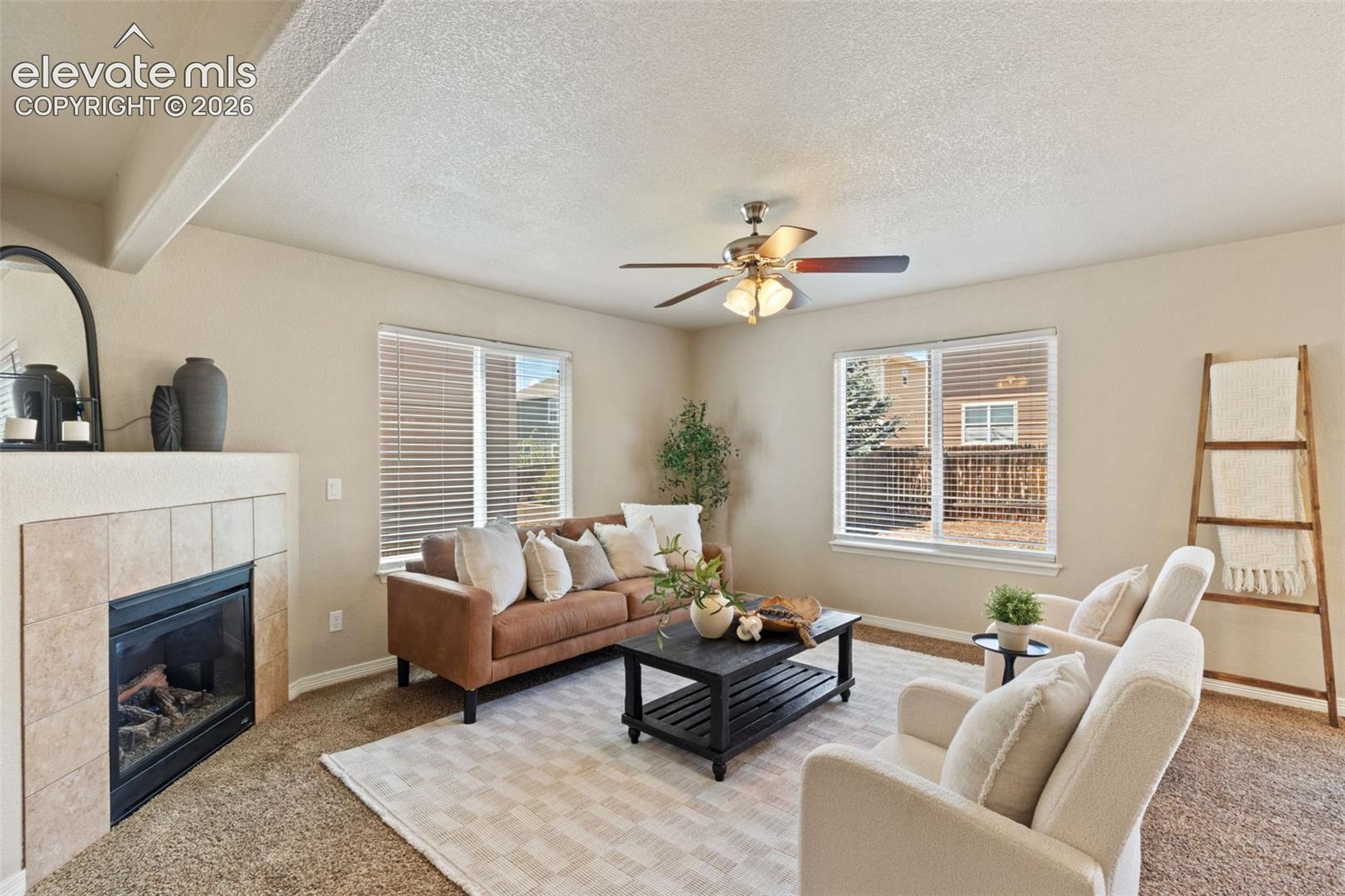 Living area featuring a tiled fireplace, multiple windows with blinds, and a ceiling fan