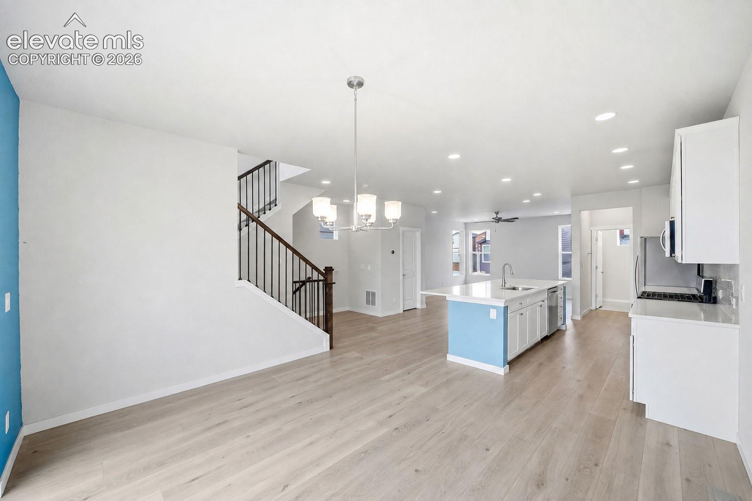 Open-concept living space featuring wood-finish flooring, a kitchen island with seating, pendant lighting, and a staircase with dark wood handrails and black balusters