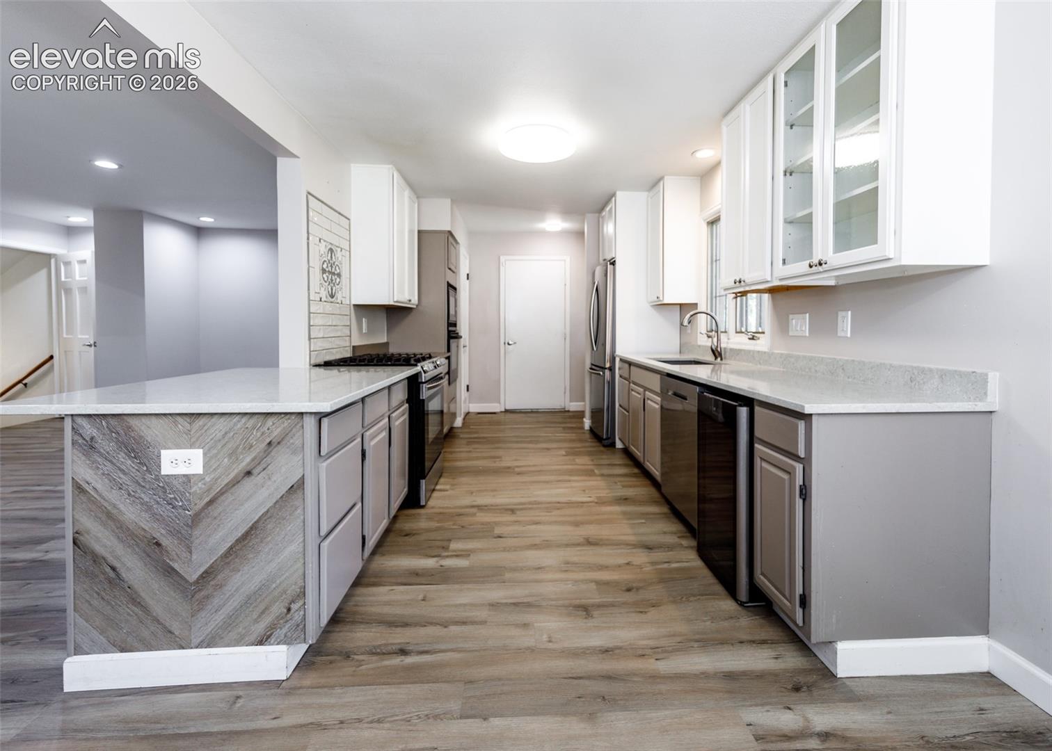 Kitchen featuring wood-finish flooring, two-tone cabinetry, stainless steel appliances, and light-toned countertops